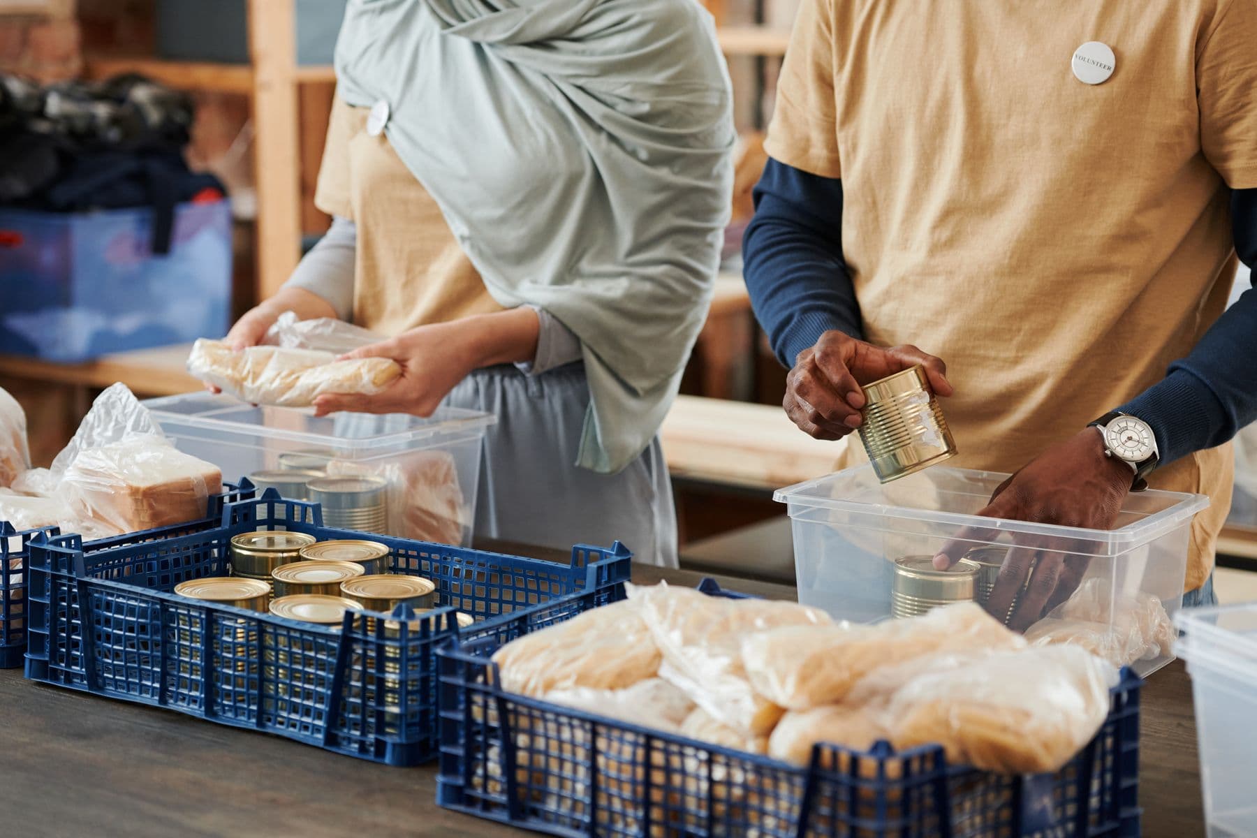 Volunteers packing bagged bread into blue crates on a long table.