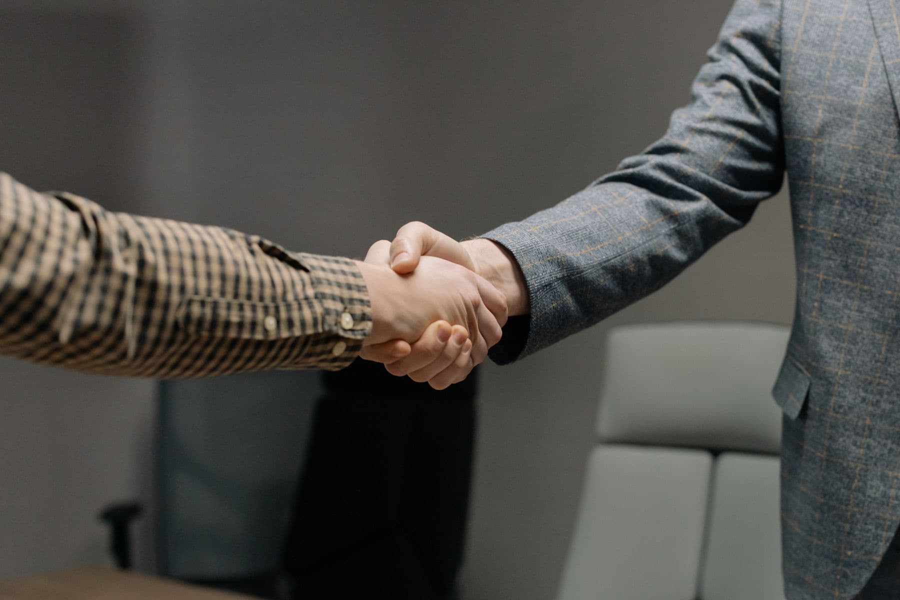 Two people shaking hands across a desk, framed on the hands.