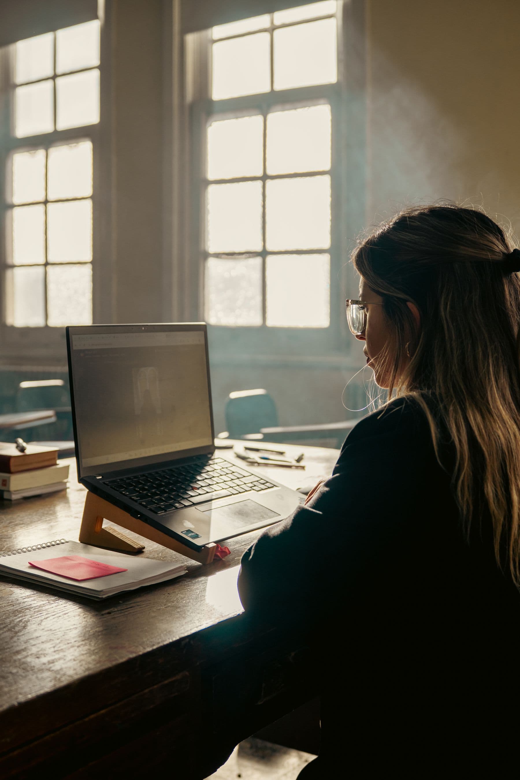 A student at a laptop and open notebook beside a stack of books.