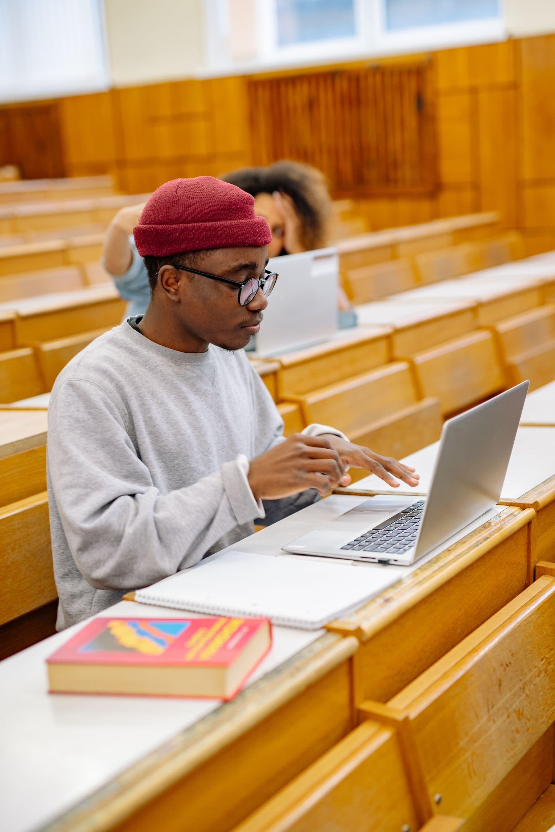 A student working at a laptop in a lecture hall, seen from the side.