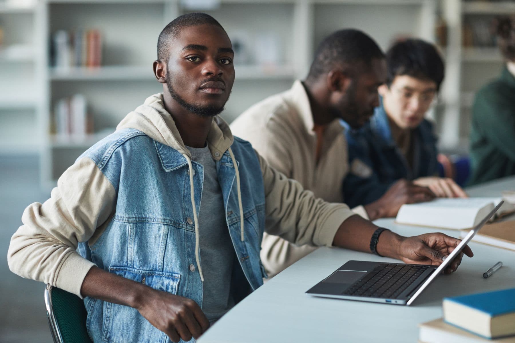 A young person working at a laptop alongside others at a shared table.